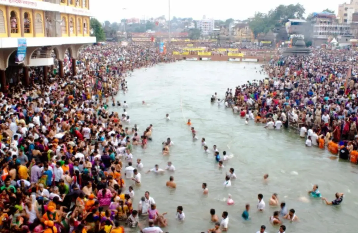 "Devotees taking a holy dip in the Godavari River during Nashik Kumbh Mela 2027 with saffron flags and saints in the background"